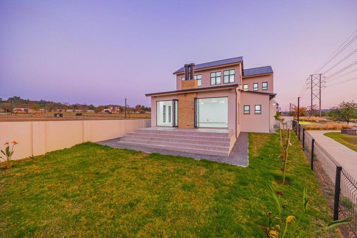 Rear view of a modern two-story house featuring a stone-clad chimney, concrete patio steps, and large bi-fold glass doors opening to a landscaped garden.