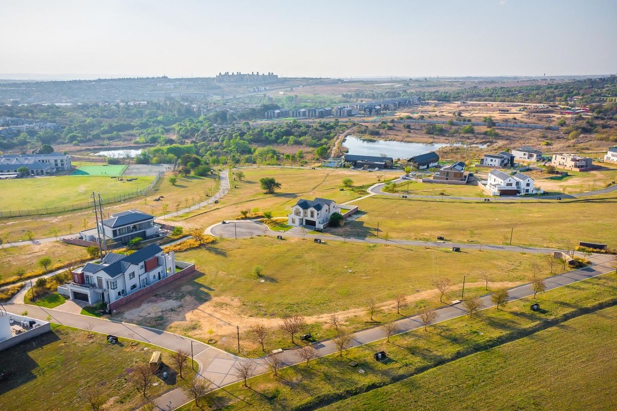 An aerial view of a residential estate featuring paved roads, open plots, and surrounding natural landscape.