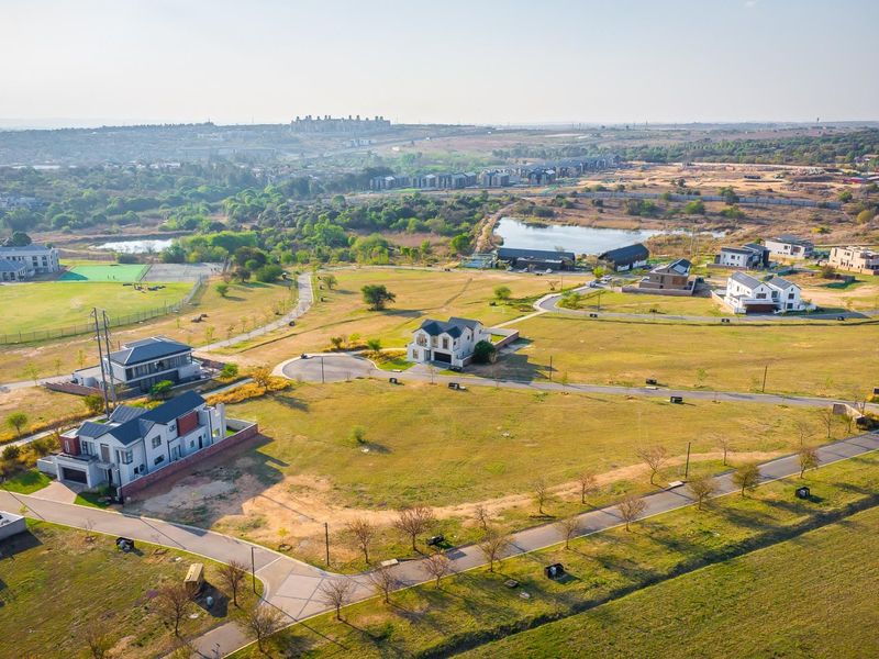 An aerial view of a residential estate featuring paved roads, open plots, and surrounding natural landscape.