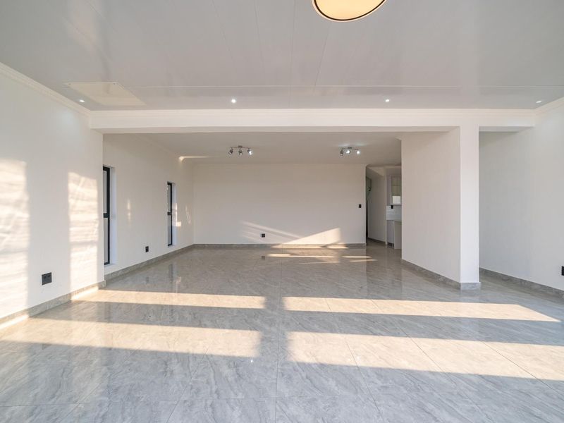 A spacious, bright open-plan living area featuring polished tiled flooring, neutral walls, and modern recessed ceiling lighting.