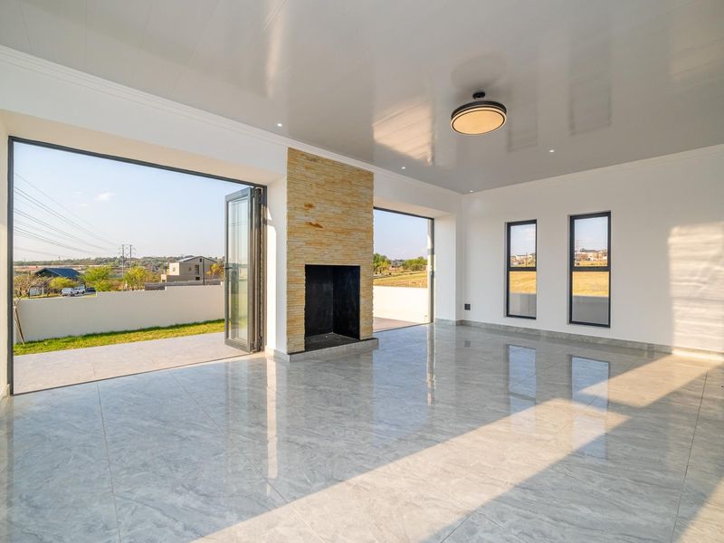Spacious, modern living area featuring polished porcelain tiles, a stone-clad fireplace, and large bi-fold doors opening to an outdoor patio with scenic views.