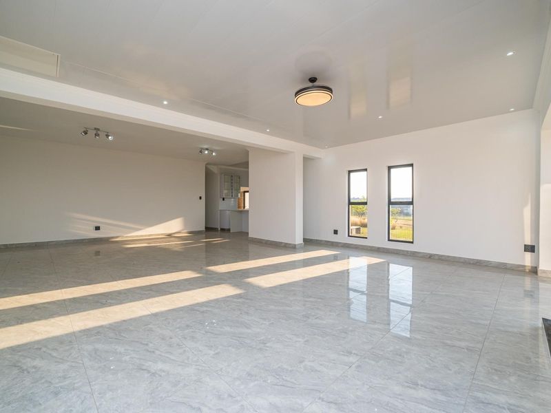Spacious open-plan living area featuring polished tile flooring, a stone-clad fireplace, and abundant natural light through modern aluminium windows.