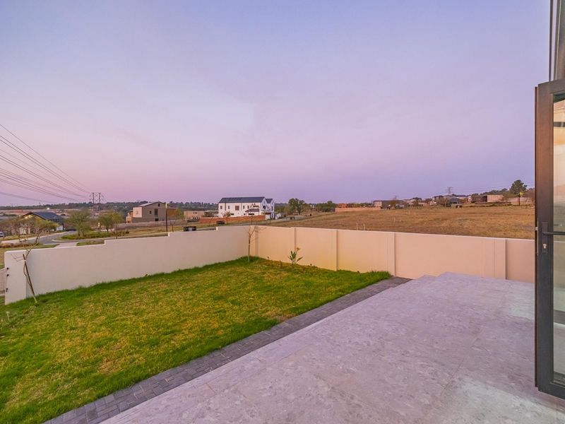A rear view of the property featuring a paved patio area, a small lawn, and a boundary wall overlooking the surrounding estate.
