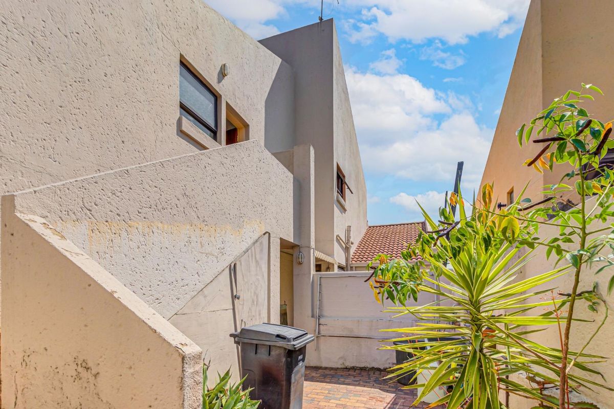 Rear exterior view of the property featuring a paved courtyard area and an external staircase leading to the upper level.