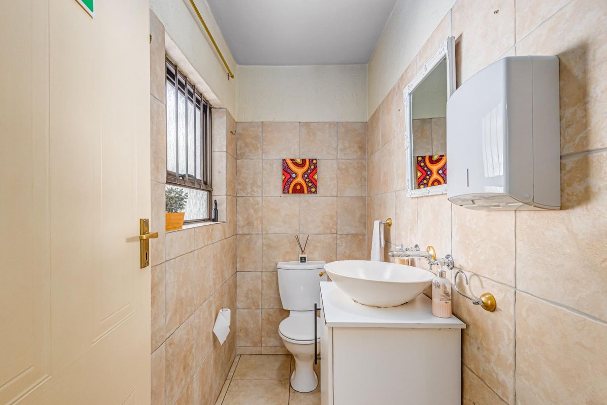 A compact bathroom featuring neutral ceramic wall and floor tiles, a modern vessel sink vanity, and a standard toilet.