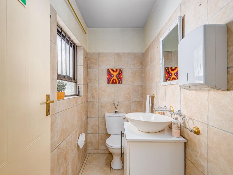 A compact bathroom featuring neutral ceramic wall and floor tiles, a modern vessel sink vanity, and a standard toilet.