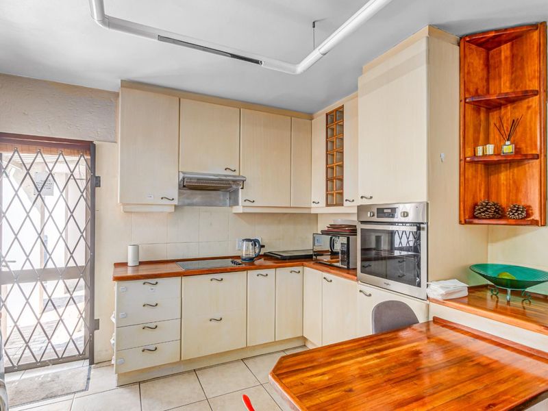 A functional kitchen featuring built-in cabinetry, wooden countertops, an integrated oven, and an electric hob, with direct access to an exterior security gate.