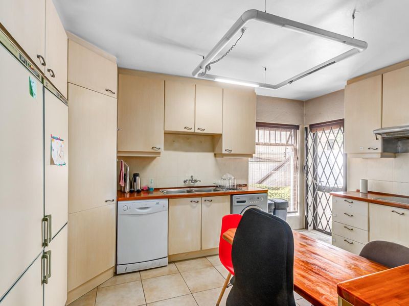 A functional kitchen featuring light-toned built-in cabinetry, laminate countertops, a double basin sink, and tiled flooring with direct access to the exterior.