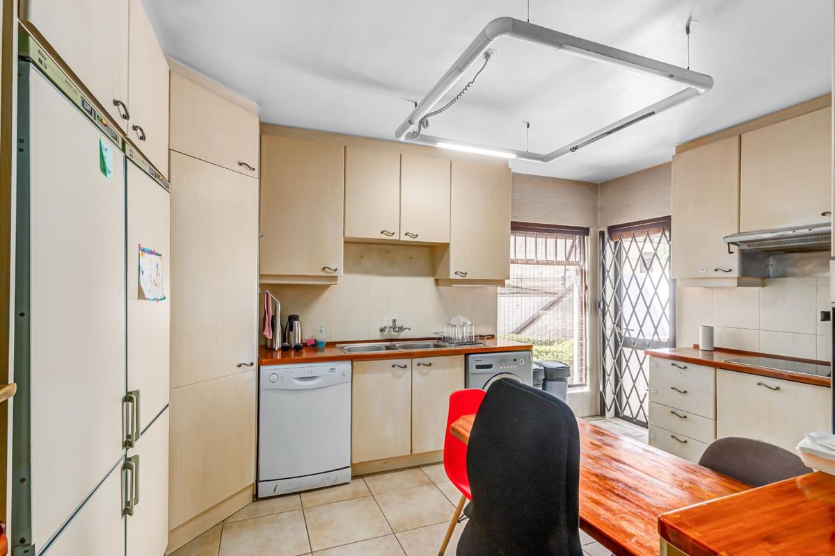 A functional kitchen featuring light-toned built-in cabinetry, laminate countertops, a double basin sink, and tiled flooring with direct access to the exterior.