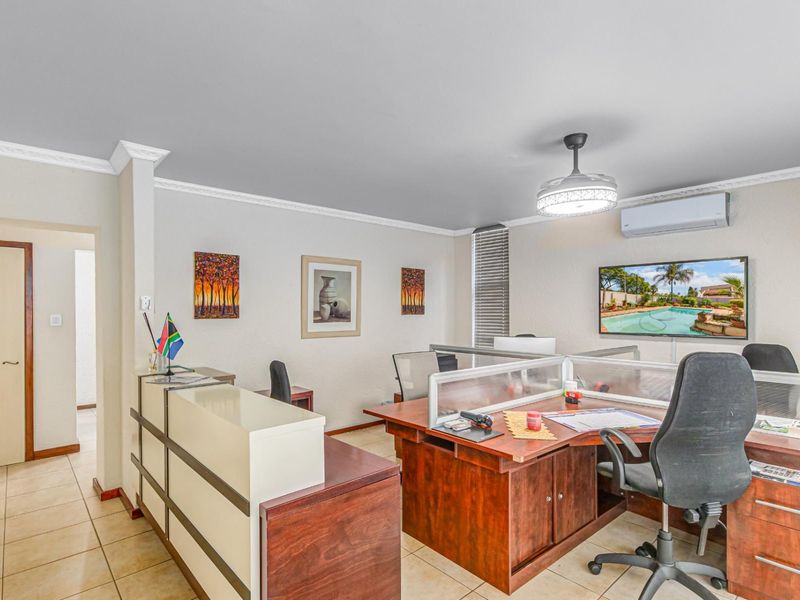 A functional office space featuring tiled flooring, a ceiling fan with integrated lighting, and a wall-mounted air conditioning unit.