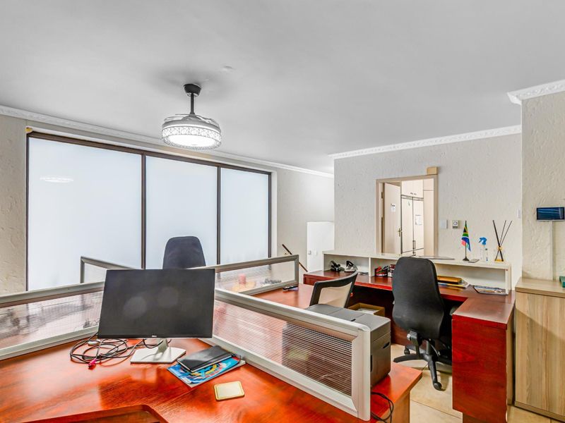 A functional office space featuring textured walls, coved cornicing, a ceiling fan, and built-in cabinetry, providing a practical work environment.