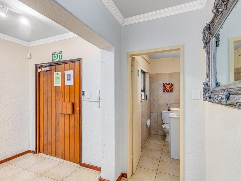 A functional hallway featuring tiled flooring, crown molding, and a wooden entrance door, with direct access to an adjacent bathroom.