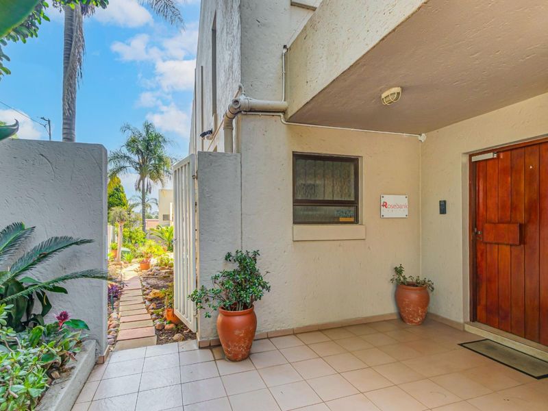 A welcoming entrance area featuring a solid wood door, tiled flooring, and a paved walkway leading through a metal gate into the garden.
