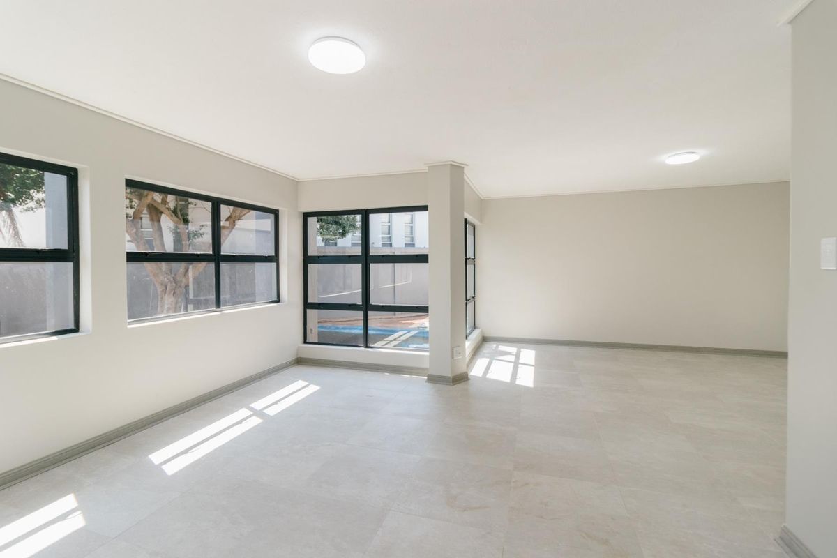 A bright, vacant living area featuring neutral tiled flooring, modern aluminium-framed windows, and clean, minimalist finishes throughout.