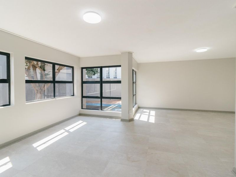 A bright, vacant living area featuring neutral tiled flooring, modern aluminium-framed windows, and clean, minimalist finishes throughout.