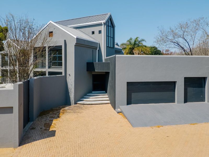 Modern architectural house exterior featuring a grey facade, double garage, and paved driveway entrance.