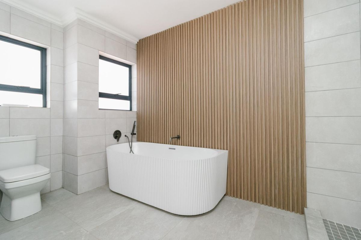 Modern bathroom featuring a contemporary freestanding bathtub, a stylish slatted wood feature wall, and neutral ceramic tiling throughout.
