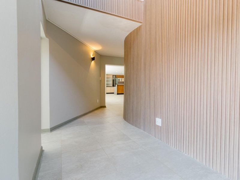 A modern, spacious hallway featuring elegant timber slat wall cladding and neutral tiled flooring, leading towards an open-plan living area.