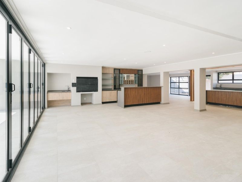 Spacious open-plan living area featuring a built-in bar, indoor braai, modern cabinetry, and large stacking glass doors leading to the exterior.