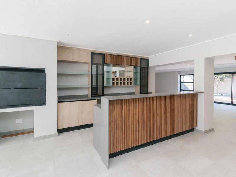 Modern, well-appointed bar area featuring custom cabinetry, a sleek bar counter, built-in wine storage, and a fireplace, finished with neutral floor tiles.