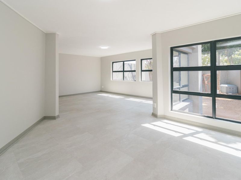 A bright, spacious, and empty living area featuring neutral tiled flooring, modern aluminium-framed windows, and clean, freshly painted walls.