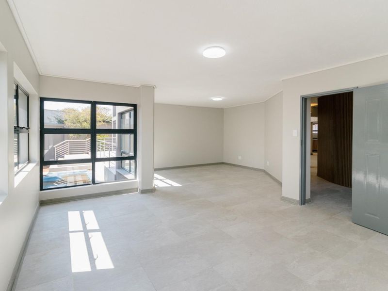 A bright, vacant living area featuring neutral tiled flooring, modern black aluminium window frames, and clean, freshly painted walls.