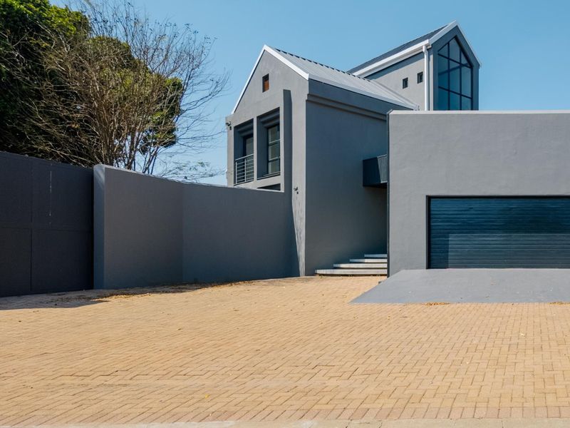 Modern architectural house exterior featuring a grey facade, paved driveway, and integrated garage, showcasing a contemporary design with clean lines.