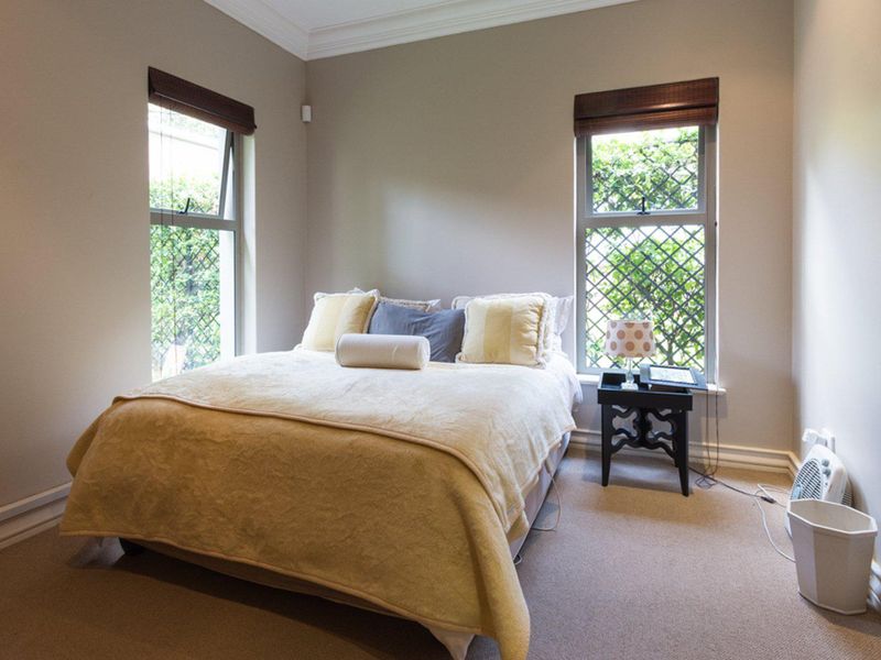 A well-maintained bedroom featuring neutral wall tones, carpeted flooring, and dual windows with security bars, providing ample natural light.