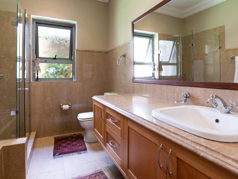 A well-maintained bathroom featuring a large vanity with stone countertop, glass-enclosed shower, and neutral wall tiling.