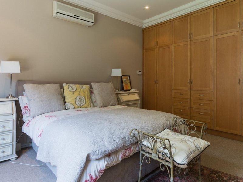 A well-maintained bedroom featuring extensive floor-to-ceiling built-in wooden cabinetry, wall-mounted air conditioning, and decorative coving.