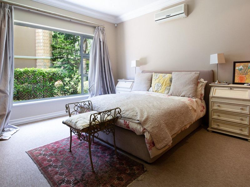 A well-maintained bedroom featuring neutral carpeting, crown molding, and a wall-mounted air conditioning unit with a view of the garden.