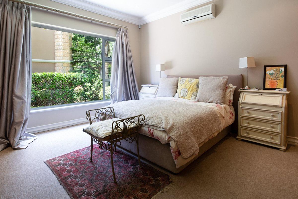 A well-maintained bedroom featuring neutral carpeting, crown molding, and a wall-mounted air conditioning unit with a view of the garden.