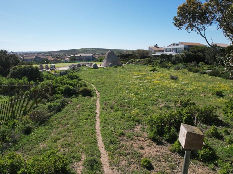 An aerial view of a vacant residential plot featuring natural rock formations, native vegetation, and perimeter fencing in a coastal estate setting.