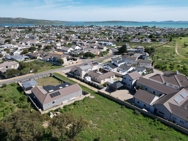 Aerial view of a residential neighborhood featuring vacant land plots and established homes with solar installations near the coast.