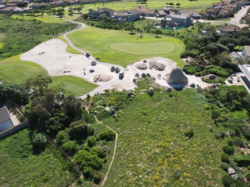 Aerial view of a vacant residential plot adjacent to a golf course, featuring natural rock formations and established coastal vegetation.