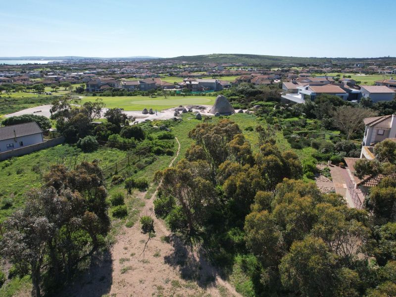 Aerial view of a vacant residential plot featuring natural vegetation, situated within a developed estate with surrounding homes and golf course views.