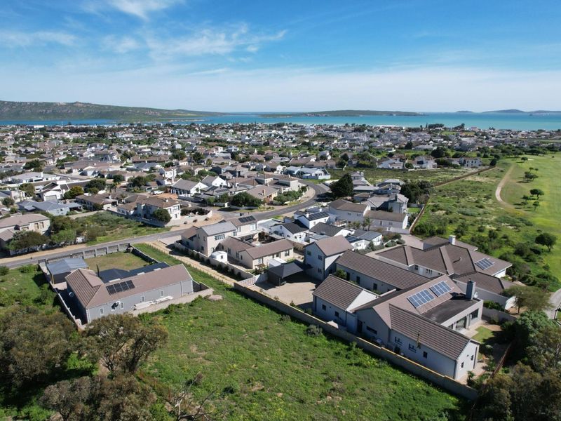 Aerial view of a residential neighborhood and vacant land plot, showcasing the surrounding coastal landscape and established housing development.
