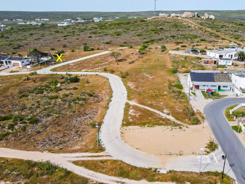 Aerial view of a residential vacant land plot situated in a coastal development with established road infrastructure and street lighting.
