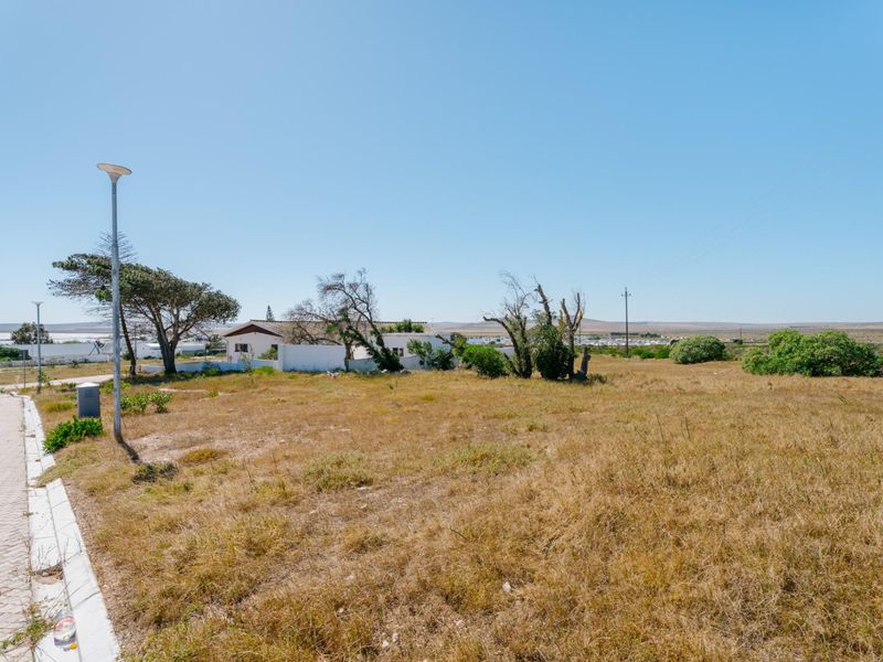 A view of a vacant residential plot featuring paved street access, kerbing, and established street lighting in a coastal setting.