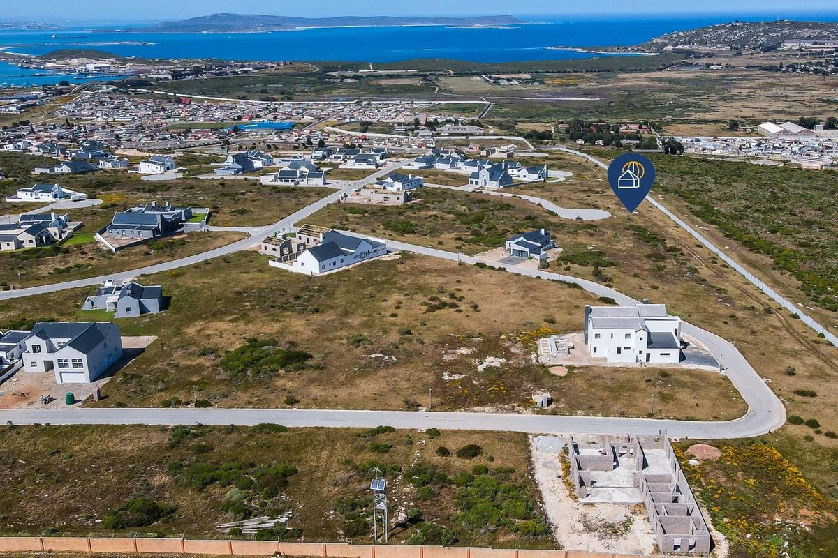 An aerial view of a residential development area featuring vacant plots, paved roads, and surrounding coastal landscape.