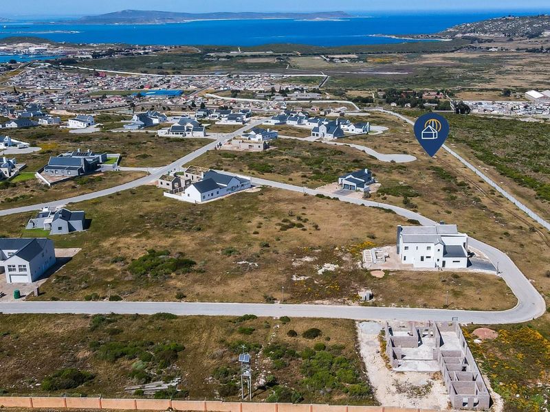 An aerial view of a residential development area featuring vacant plots, paved roads, and surrounding coastal landscape.