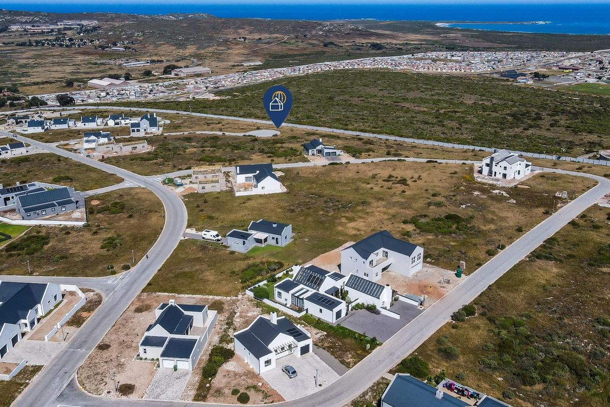 An aerial view of a residential development area featuring vacant plots and established modern homes with coastal surroundings.