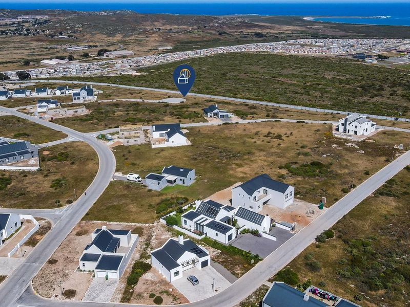 An aerial view of a residential development area featuring vacant plots and established modern homes with coastal surroundings.