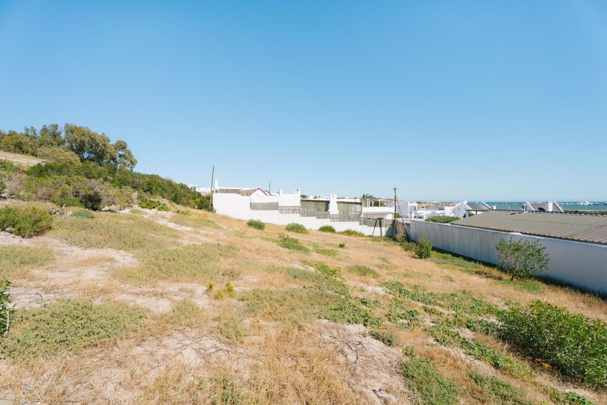 A view of a vacant residential plot featuring sloped terrain and a boundary wall, situated in a coastal neighborhood.