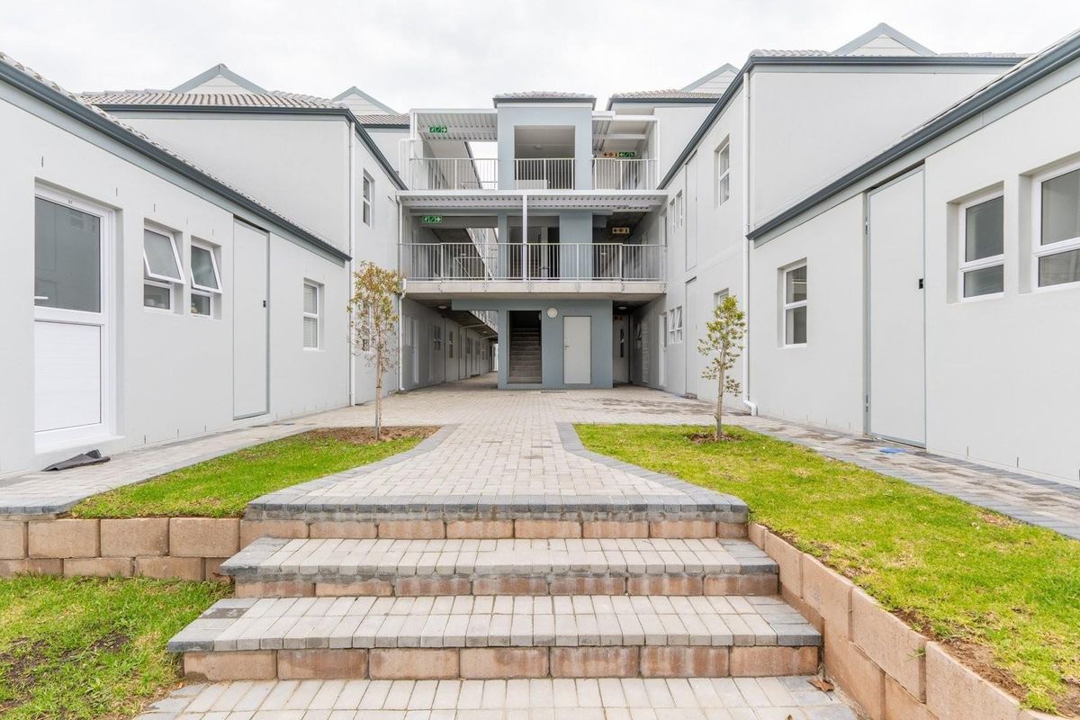 A view of the apartment complex courtyard featuring paved walkways, landscaped grass areas, and multi-level balcony access.