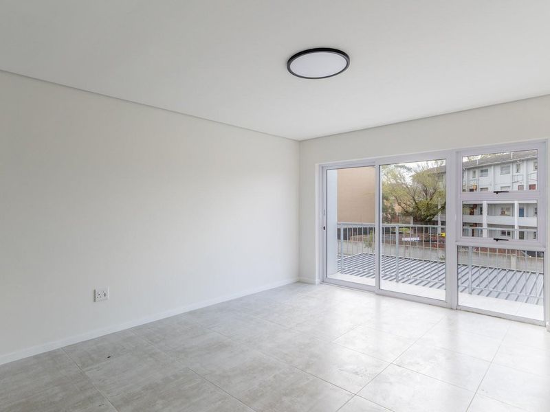 A bright, empty living area featuring modern tiled flooring, a flush mount ceiling light, and a large sliding glass door leading to a balcony.
