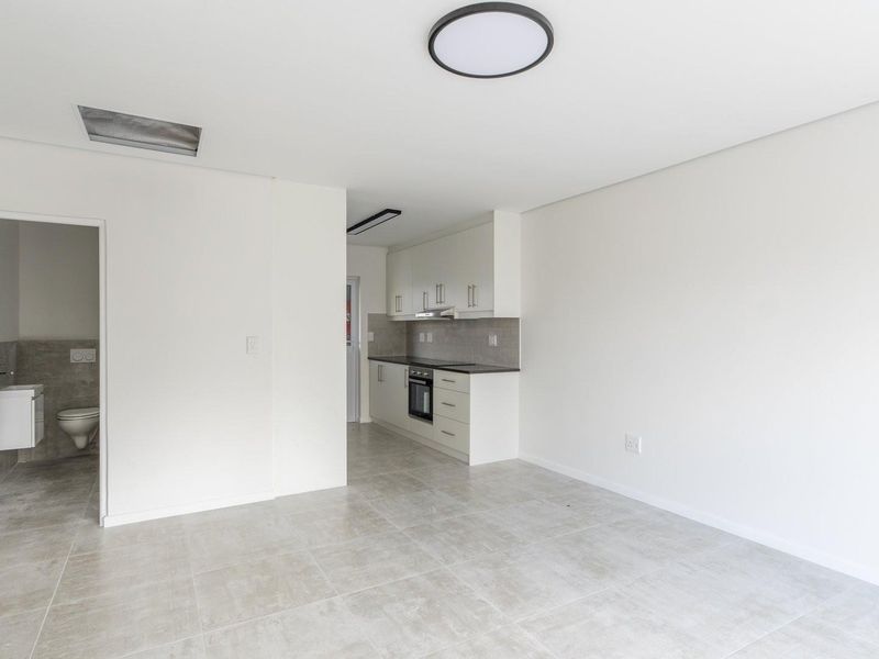 Modern open-plan living area featuring tiled floors, a sleek kitchen with built-in appliances, and an adjacent bathroom with contemporary fixtures.