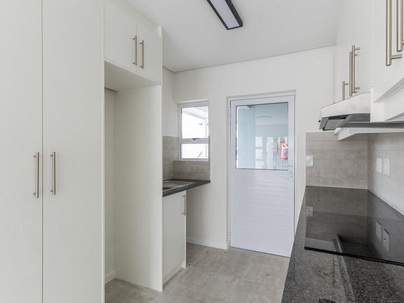 Modern kitchen featuring white cabinetry, dark granite countertops, integrated electric hob, extractor fan, and tiled finishes with direct exterior access.