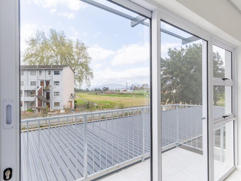 A bright, modern balcony featuring tiled flooring, a secure metal balustrade, and large sliding glass doors offering an open view of the surrounding area.