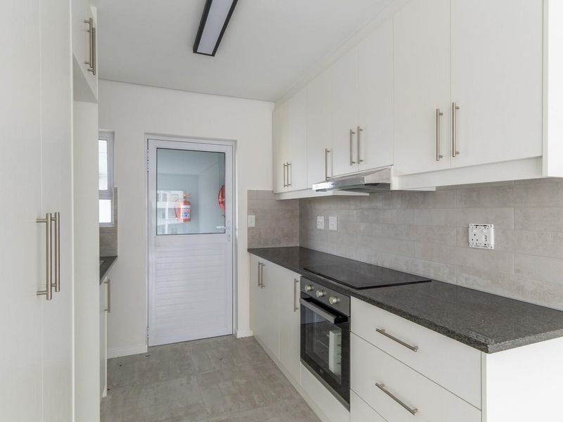 Modern kitchen featuring white cabinetry, dark stone countertops, integrated oven and hob, tiled backsplash, and direct access to an exterior area.